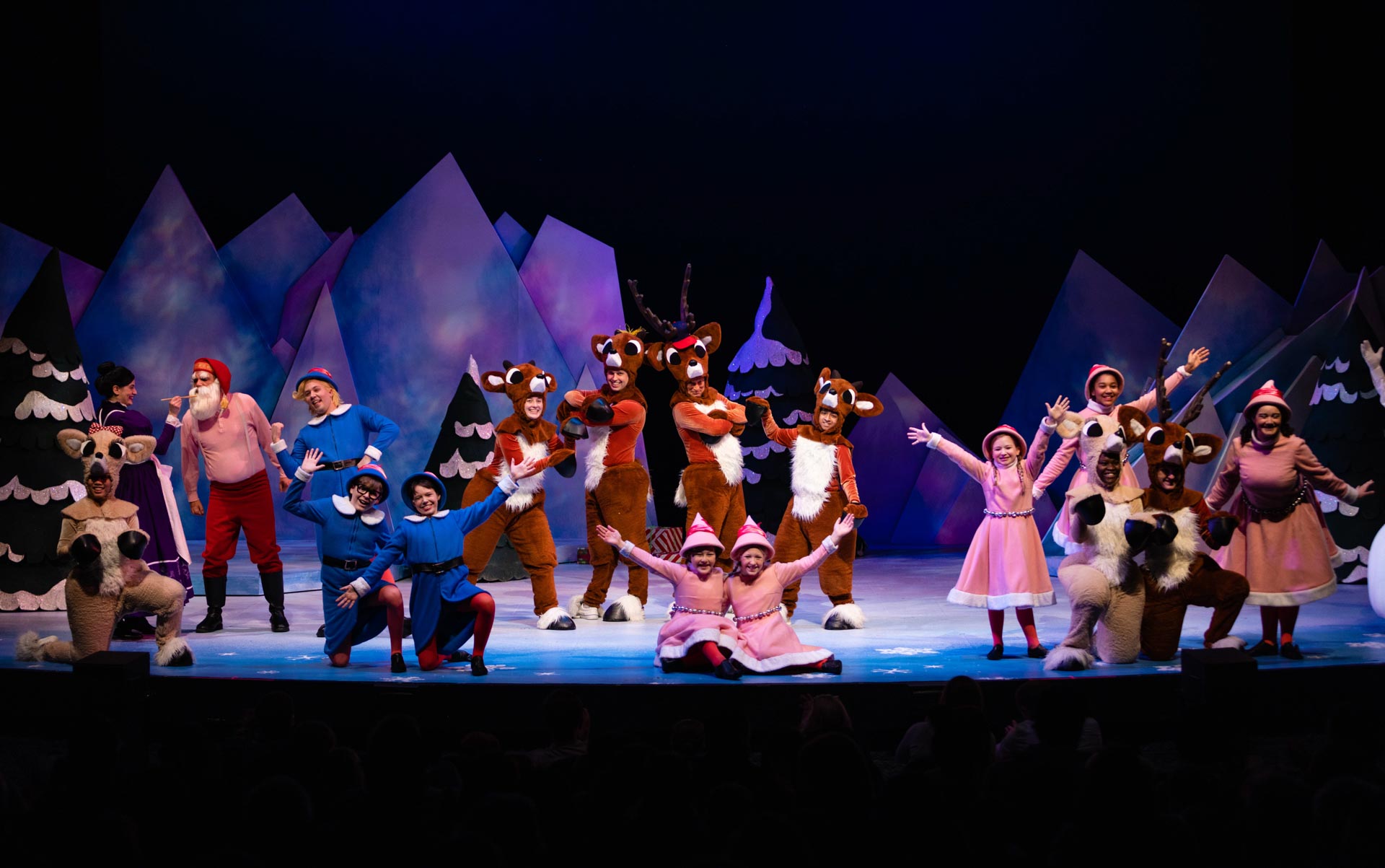 A photo of actors in costumes on stage with colorful lights performing in Rudolph the Red-Nosed Reindeer: The Musical at Stages Theatre Company
